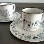 Platos y tazas blancos de cerámica con ilustraciones en color negro con motivos de naturaleza