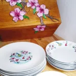 Platos apilados con ilustraciones hechas a acuarela y una caja para guardarlos al fondo